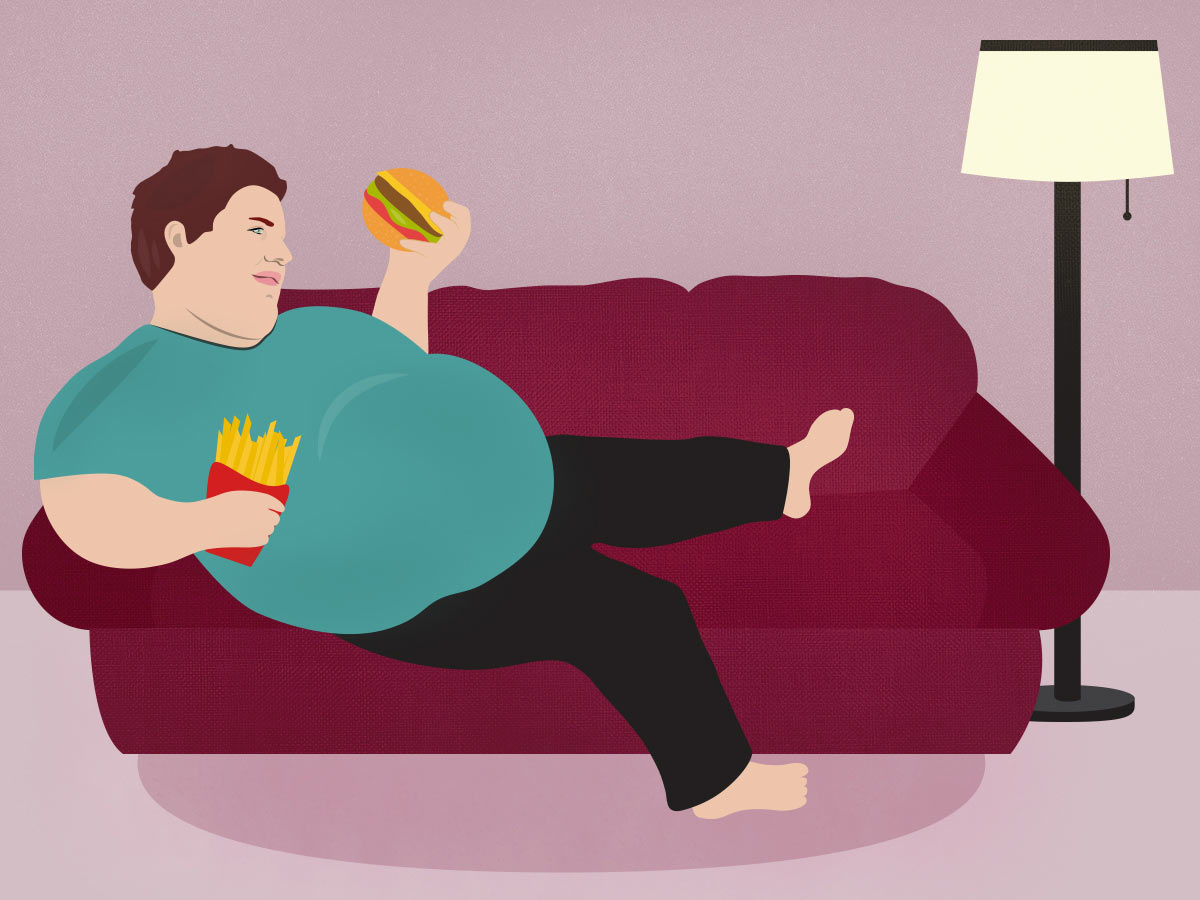 Obese man sitting on a sofa holding burger and french fries