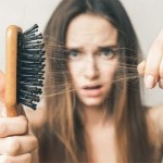 A lady pulling her hair out of her brush shocked from losing lots of hair strands